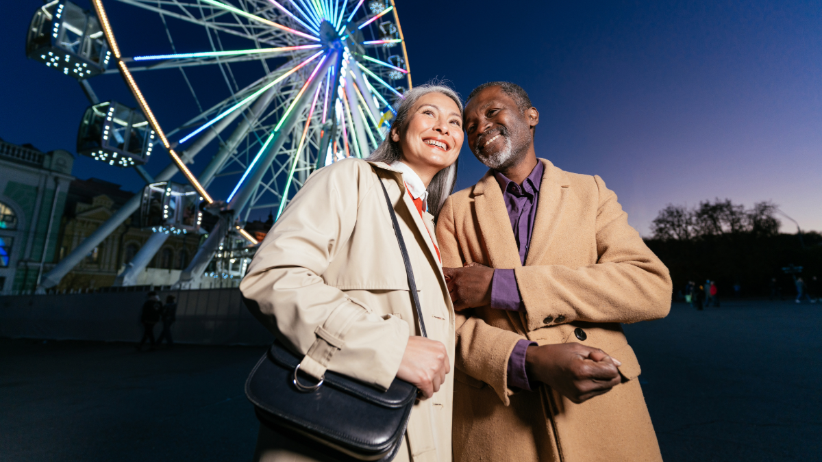 a woman and man out at night holding hands, standing in front of a ferris wheel - they're enjoying their evening because they have taken steps to support their financial independence in their later years