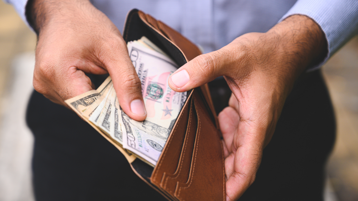 A man's hands holding open his wallet to show several U.S. bills - his decisions on health care expenses help determine how much money he has in his wallet