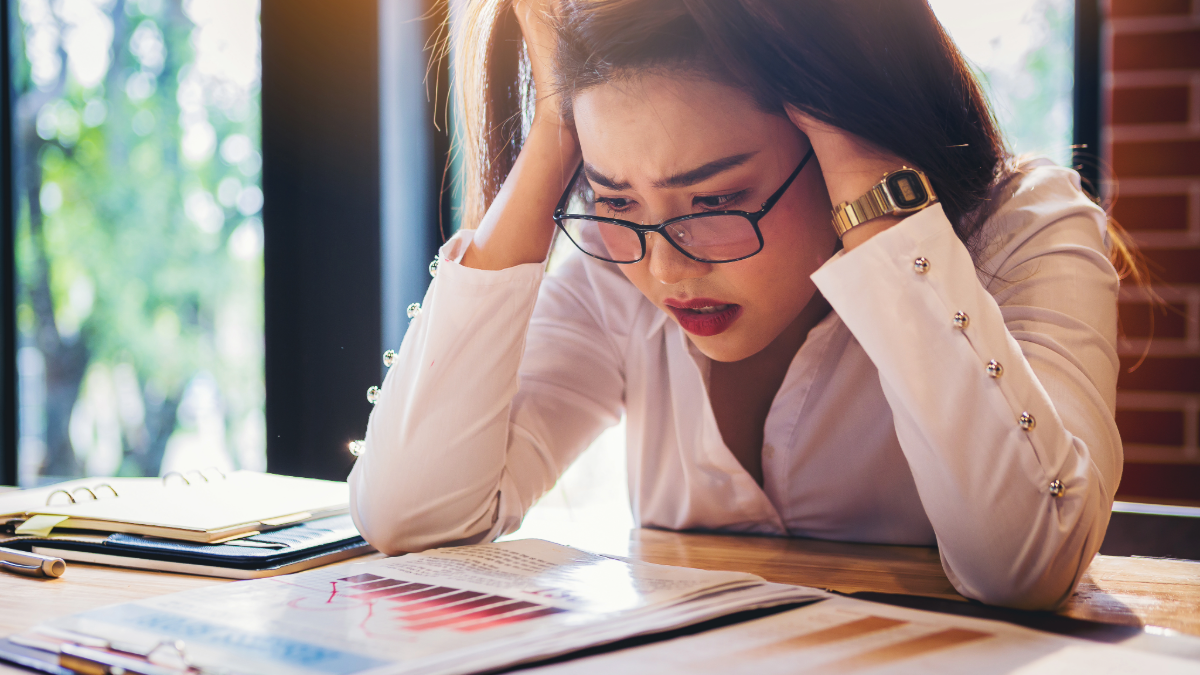 woman holding her head in her hands with a frustrated look while looking at financial graphs